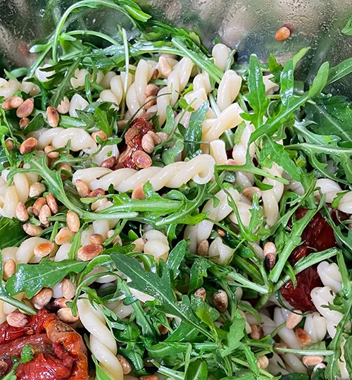 Rucola-Salat mit weißen Bohnen und getrockneten Tomaten - gesundes Rezept Frischer Rucola-Salat mit weißen Bohnen, getrockneten Tomaten und Pinienkernen auf einem Teller