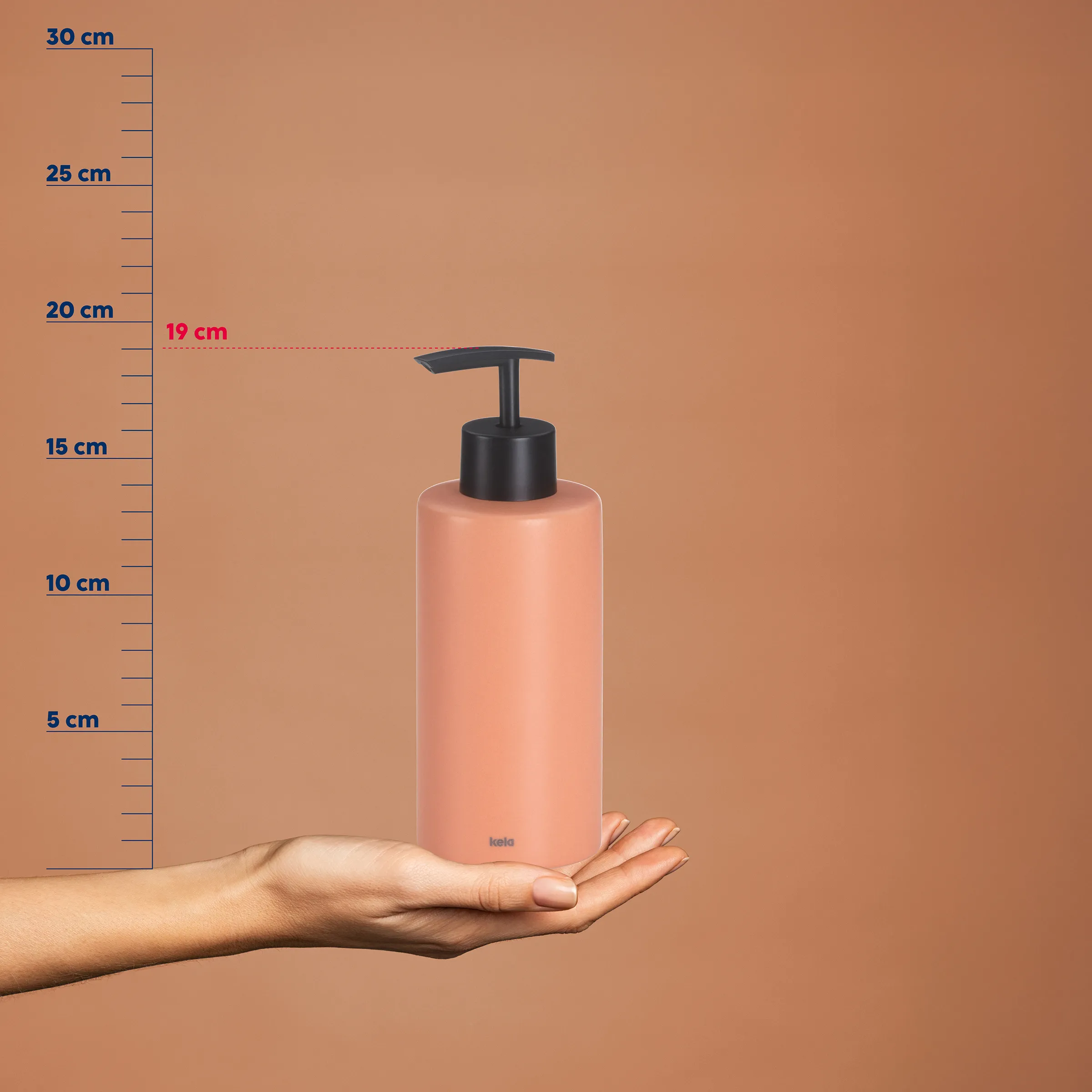 Seifenspender rosa 19 cm mit Pumpe - Kela Badezimmer Dispenser Rosa Seifenspender mit schwarzer Pumpe, 19 cm hoch, auf Hand vor Messskala auf beigem Hintergrund