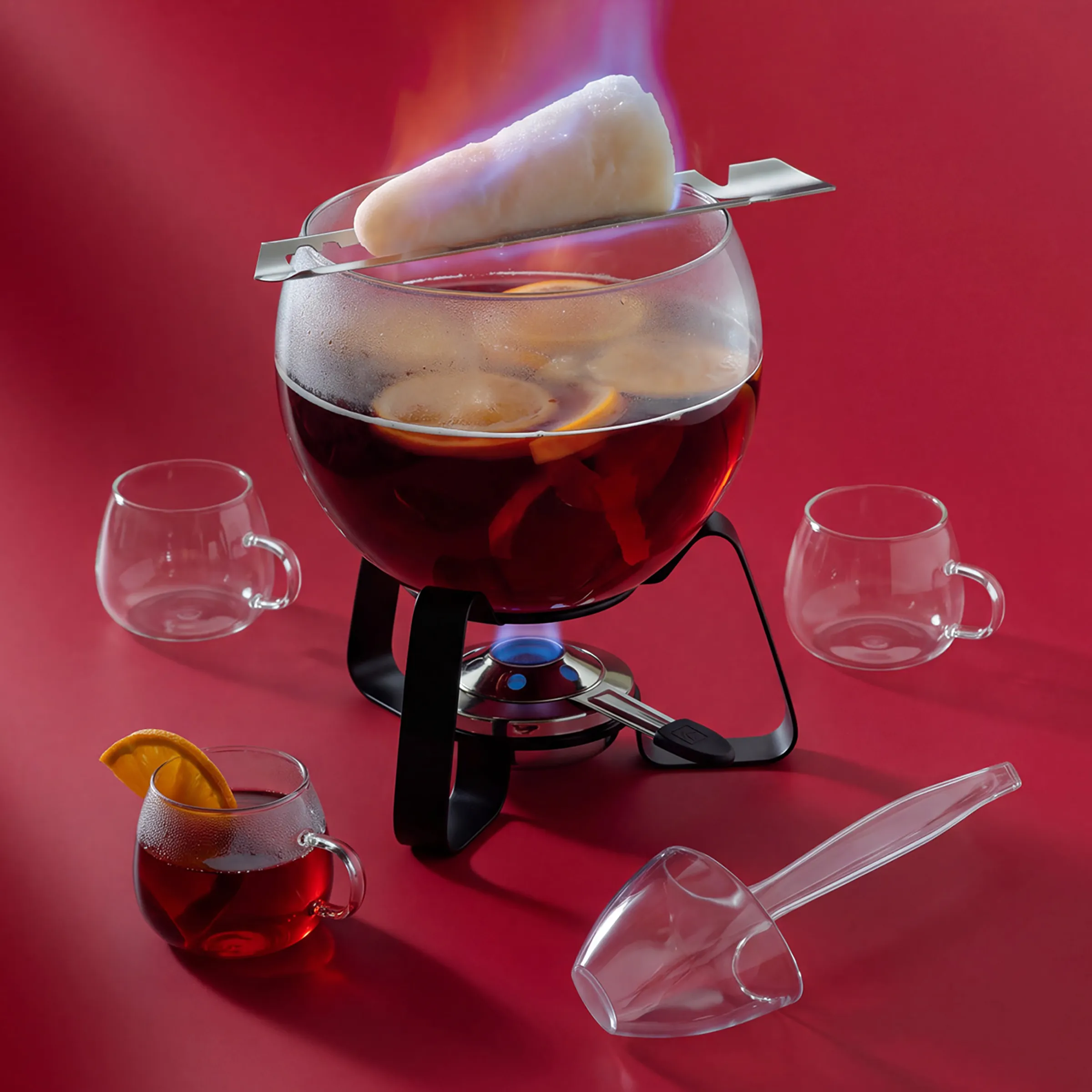 Fondue-Set Gusseisen - Klassisches Fondue Zubehör Schwarze Fondue-Set mit großem Topf, Stövchen und Brenner, umgeben von leeren Tassen und Gabel auf Holztisch vor rotem Hintergrund.