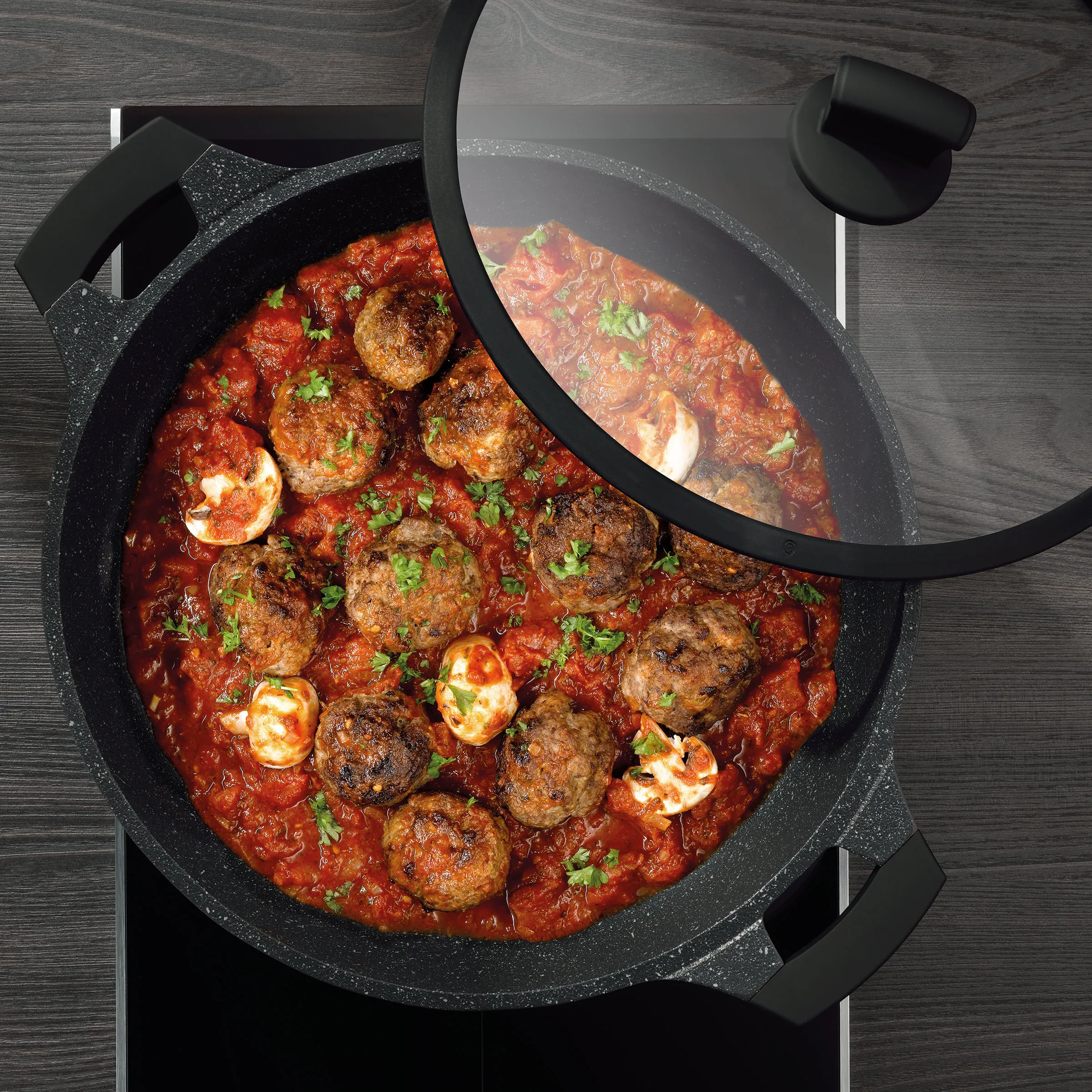 Fleischbällchen in Tomatensoße - leckeres Rezept im Topf Schwarzer Topf mit Deckel auf Holztisch, gefüllt mit Fleischbällchen in roter Tomatensoße, garniert mit Petersilie und Mozzarella