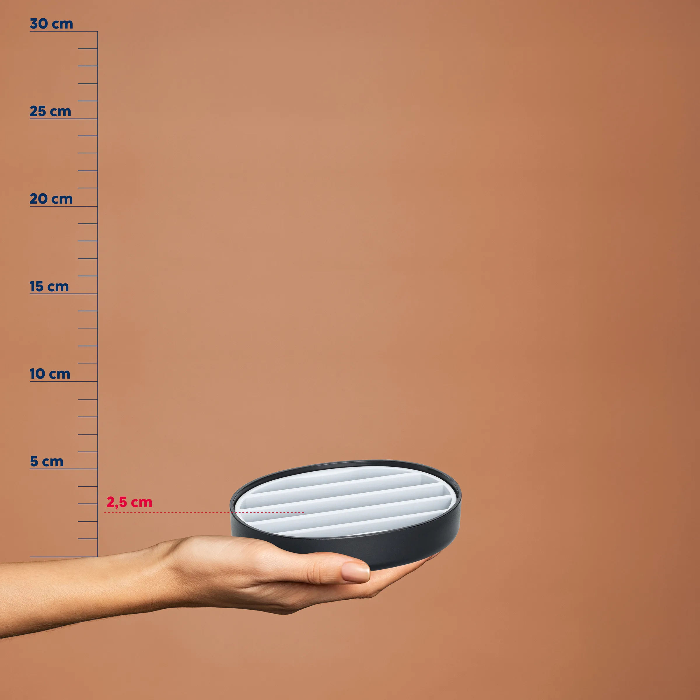 Hand hält schwarze runde Dose mit weißem Deckel vor Maßstab, Höhe 2,5 cm