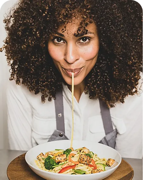 Woman eating Asian noodles - Healthy cuisine Woman with curly brown hair eating noodles with vegetables from a white plate using chopsticks.