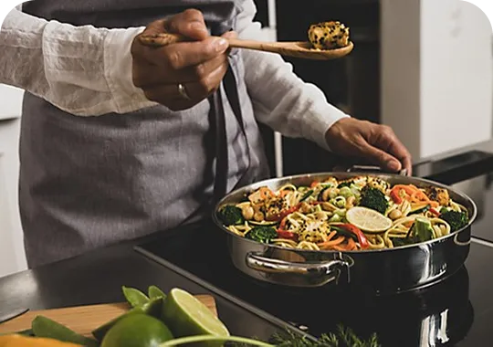 Asian Wok Noodles - Professional Cooking Chef serves Asian fusion cuisine from black wok with noodles, vegetables and lime on stovetop
