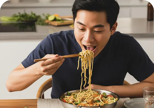 Man eating noodles - Asian cuisine Man in dark shirt eating noodles with chopsticks from a bowl in modern kitchen