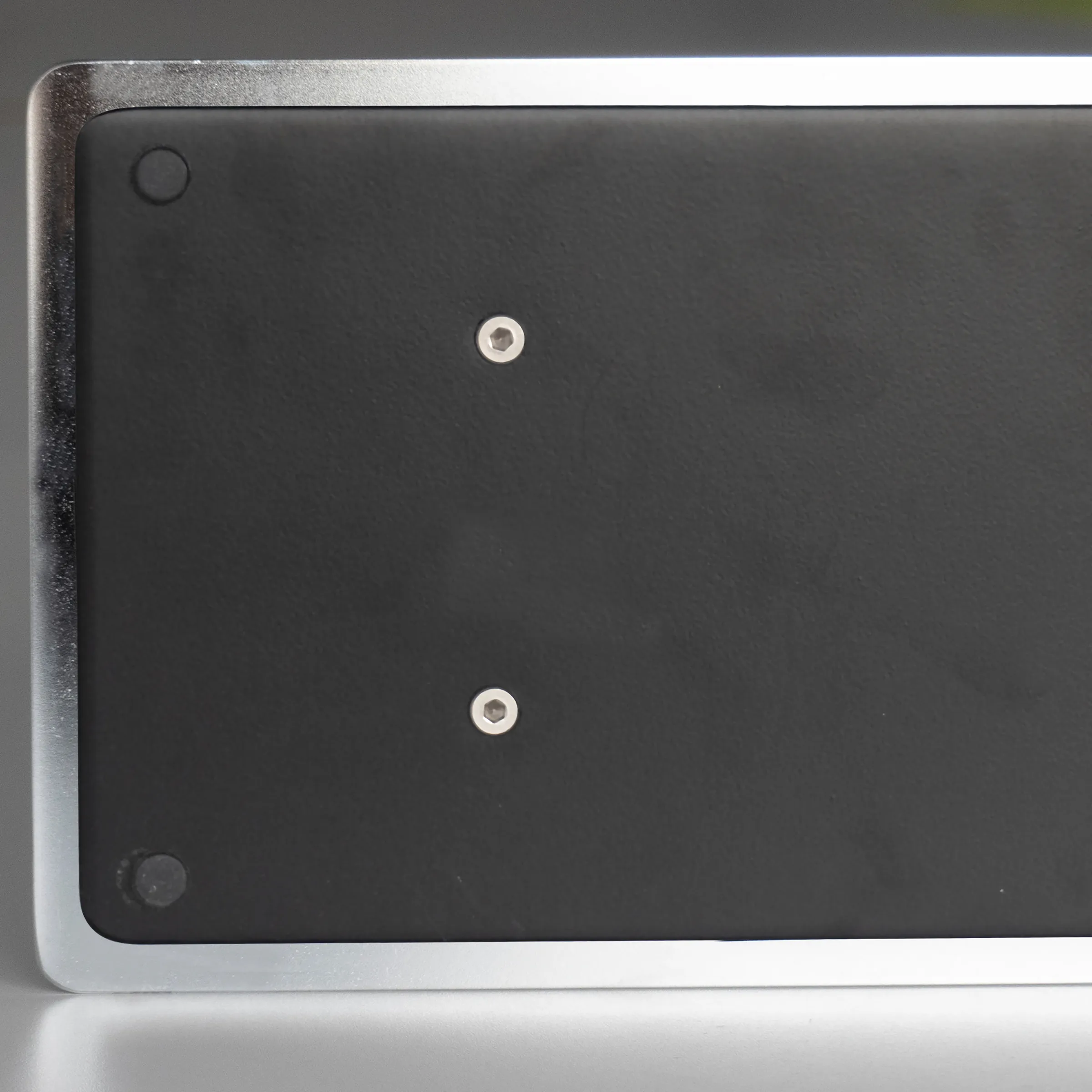 Schwarze Laptop-Unterseite mit Metallrahmen und zwei silbernen Befestigungsschrauben