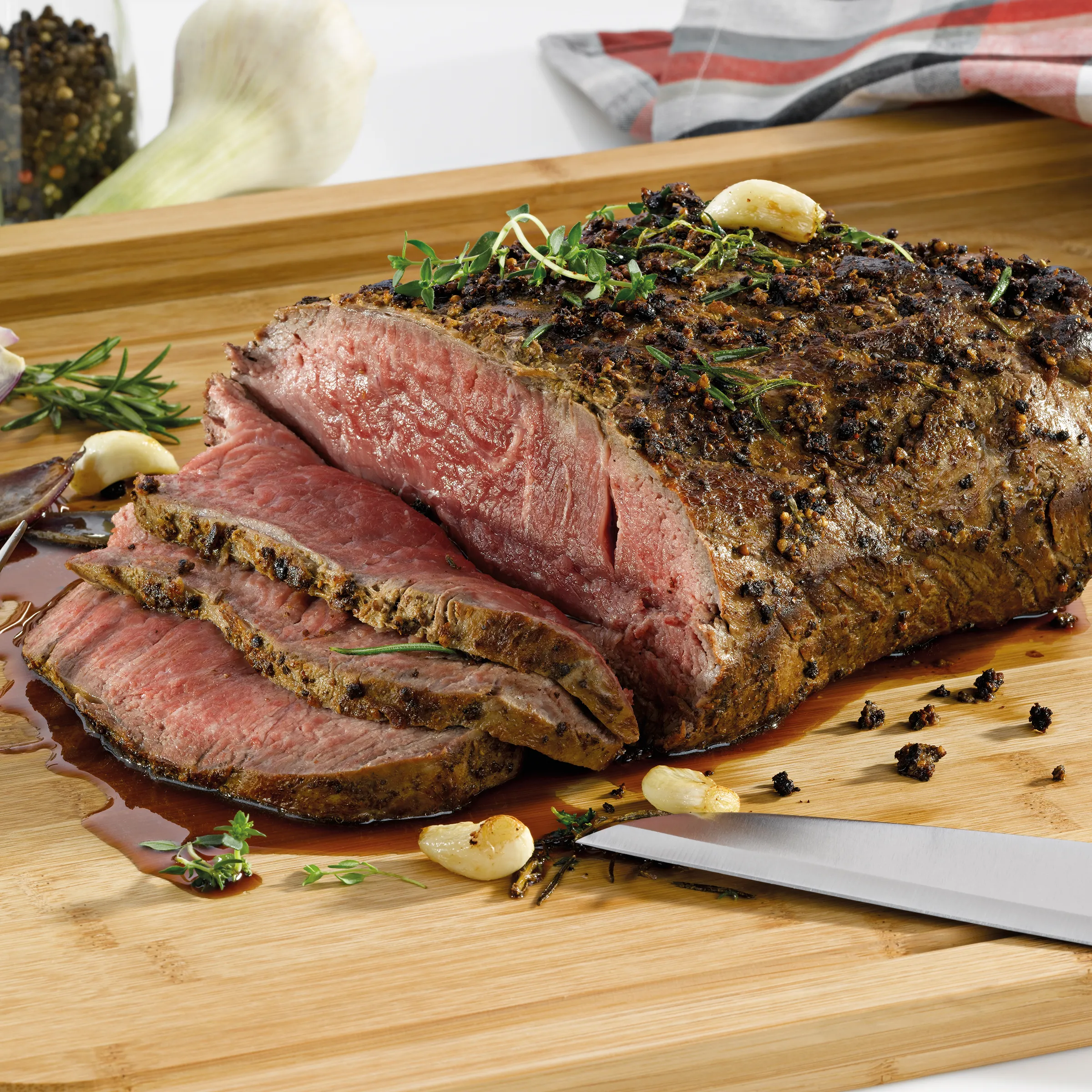 Roastbeef medium-rare gebraten mit Kräuterkruste und Knoblauch Gebratenes Roastbeef medium-rare aufgeschnitten auf Holzbrett mit Knoblauch, Kräutern und Gewürzen