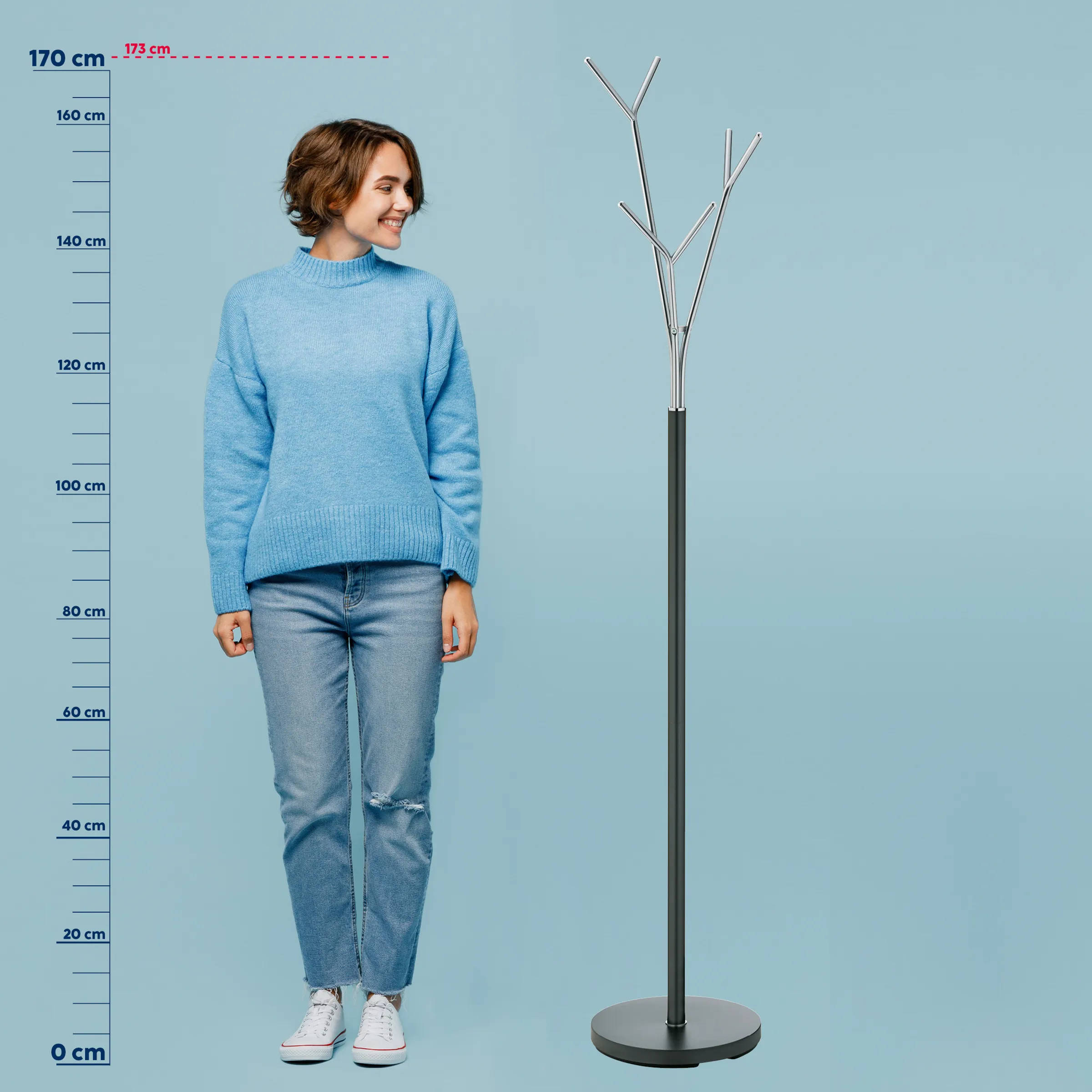 Frau in blauem Pullover und Jeans neben schwarzer Stehleuchte mit Metallästchen auf hellblauem Hintergrund. Höhenvergleich bis 173 cm.