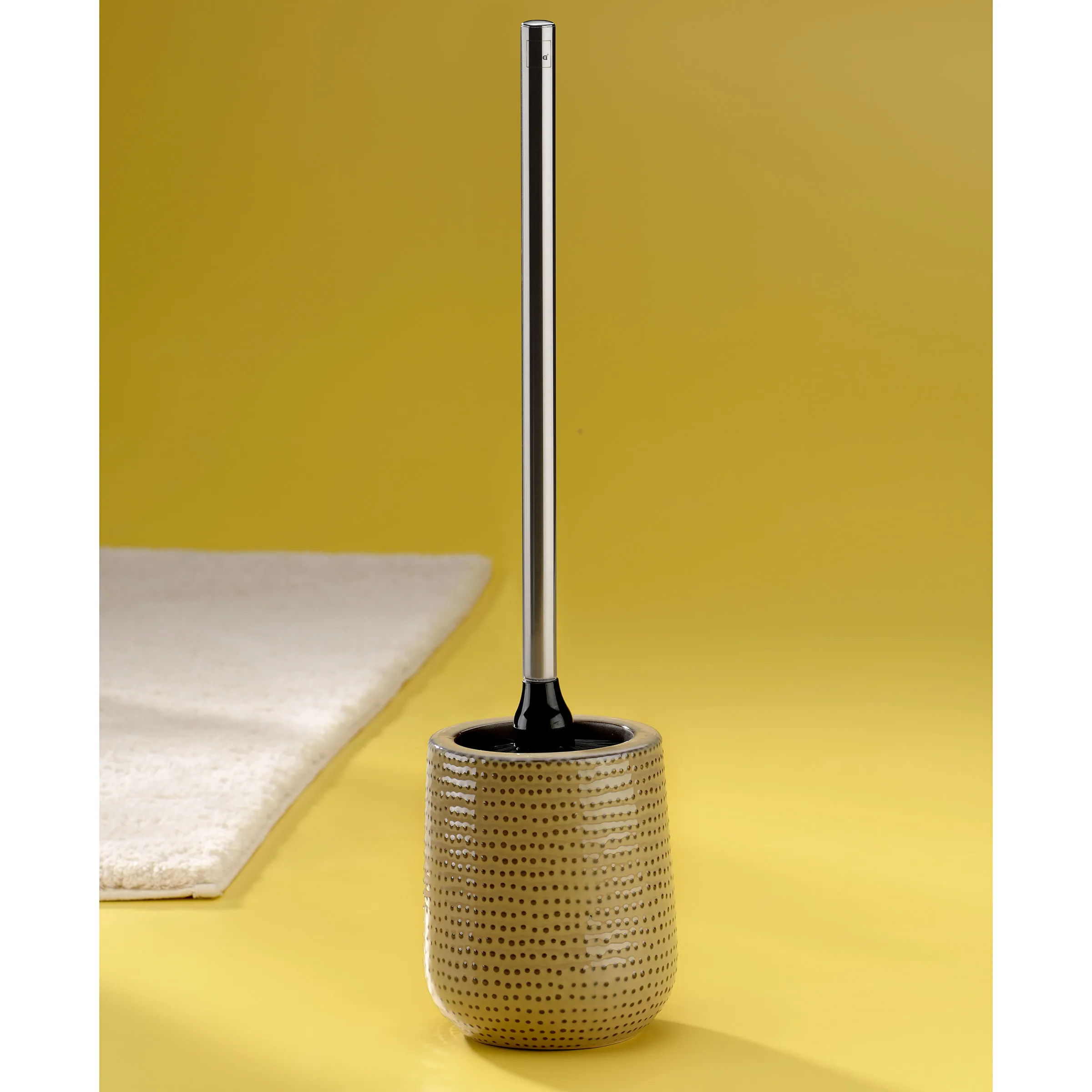 Toilettenbürste mit Behälter - Moderne WC-Bürste Graue Toilettenbürste mit perforiertem Behälter und schwarzem Griff auf gelbem Hintergrund neben weißem Handtuch