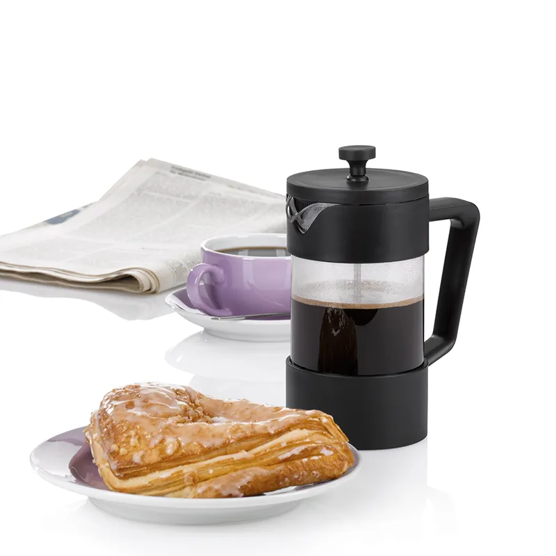 French Press Kaffeebereiter mit Frühstück - Kaffeezubereitung Schwarze French Press mit Kaffee neben lila Tasse und glasiertem Gebäck auf weißem Teller, Zeitung im Hintergrund