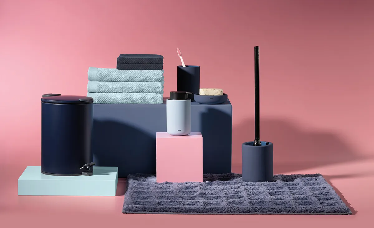 Badezimmer-Accessoires-Set in Dunkelblau mit Handtüchern, Seifenspender, WC-Bürste und Mülleimer auf rosa Hintergrund