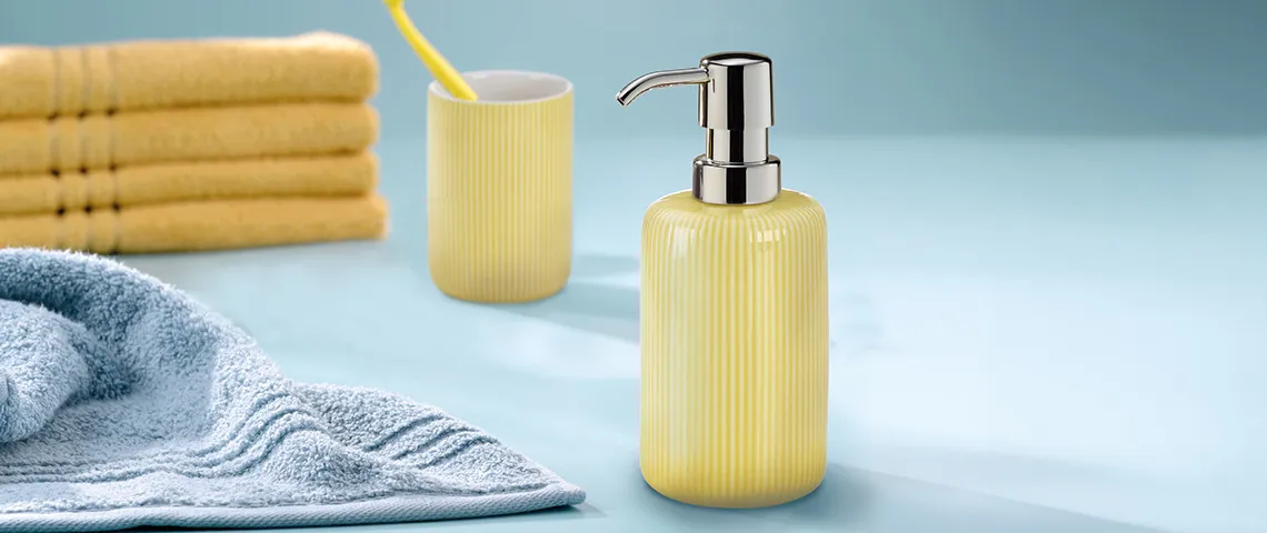 Badezimmer-Set mit gelber Seifenspender, Zahnbürstenbecher, gelben Handtüchern und blauem Handtuch auf hellblauem Hintergrund.