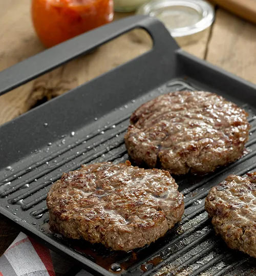 Fleischpflanzerl braten - Rezept mit Hackfleisch Drei gebratene Fleischpflanzerl auf schwarzem Grill-Tablett, mit Soße im Hintergrund