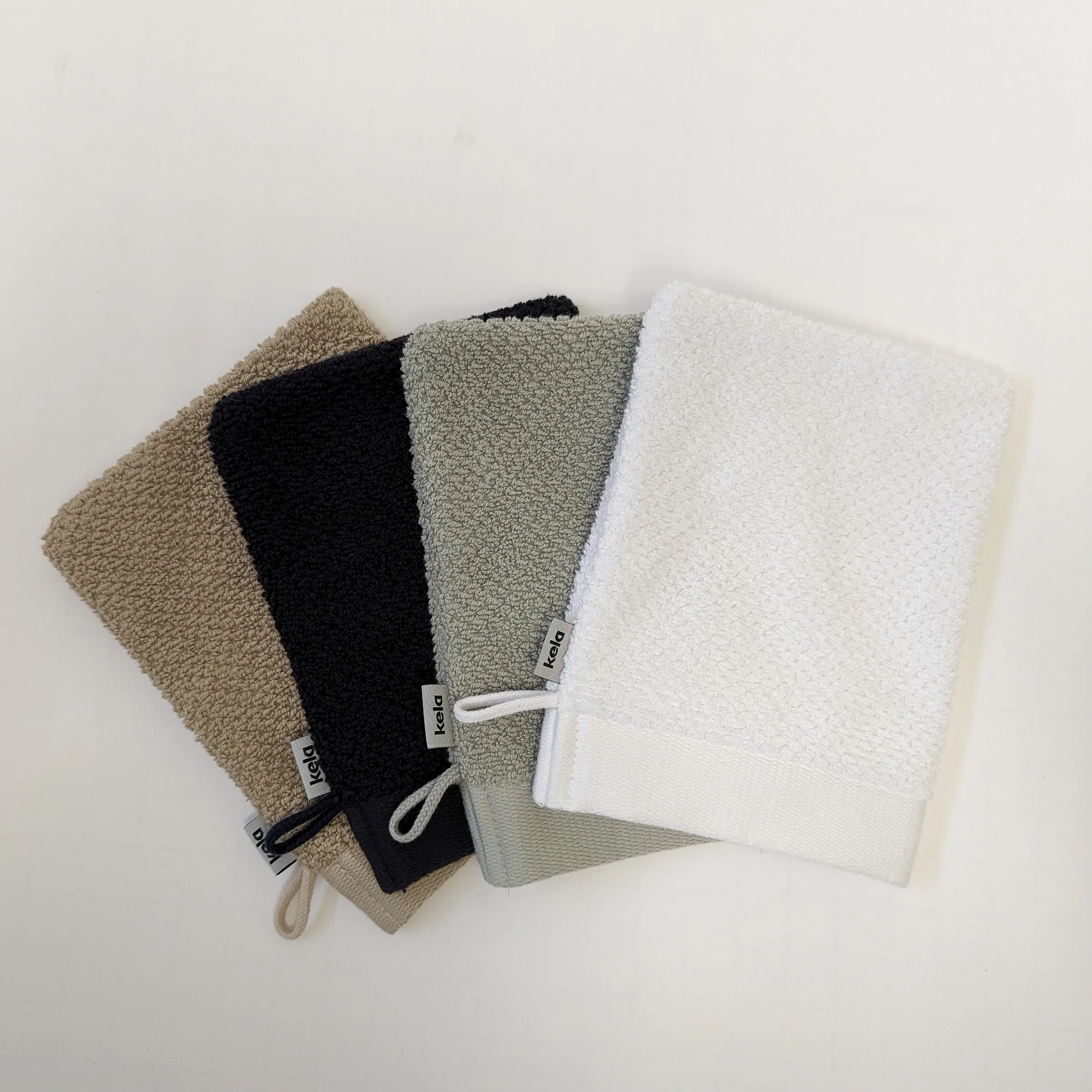 kela Waschlappen Set - 4 Waschhandschuhe in verschiedenen Farben Vier Waschlappen von kela in beige, schwarz, salbeigrün und weiß mit Aufhängeschlaufen auf hellem Hintergrund