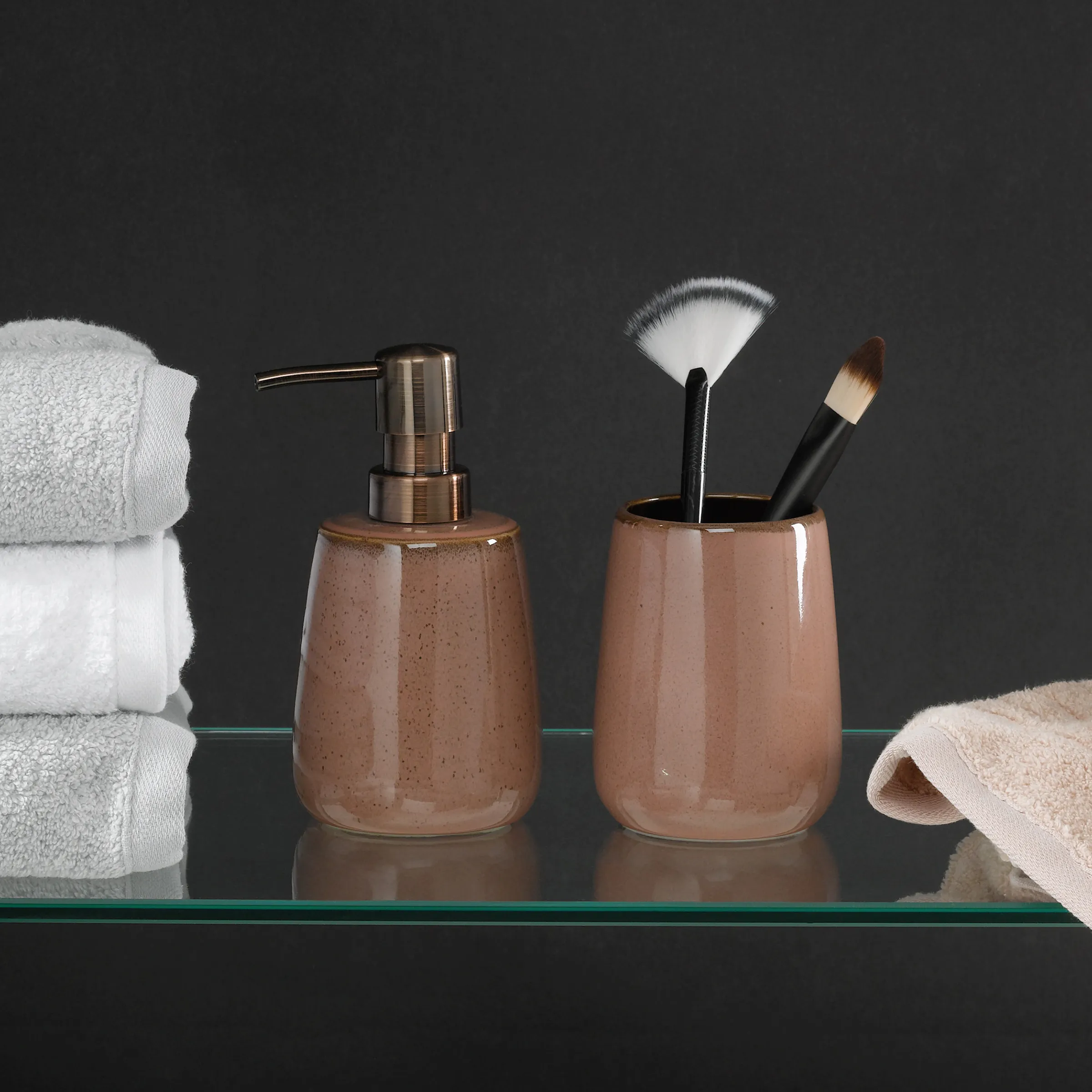 Badezimmer-Accessoires Set braun mit Seifenspender und Kosmetik-Becher Braunes Badezimmer-Set mit Seifenspender und Becher mit Make-up-Pinseln neben weißen Handtüchern auf Glasregal