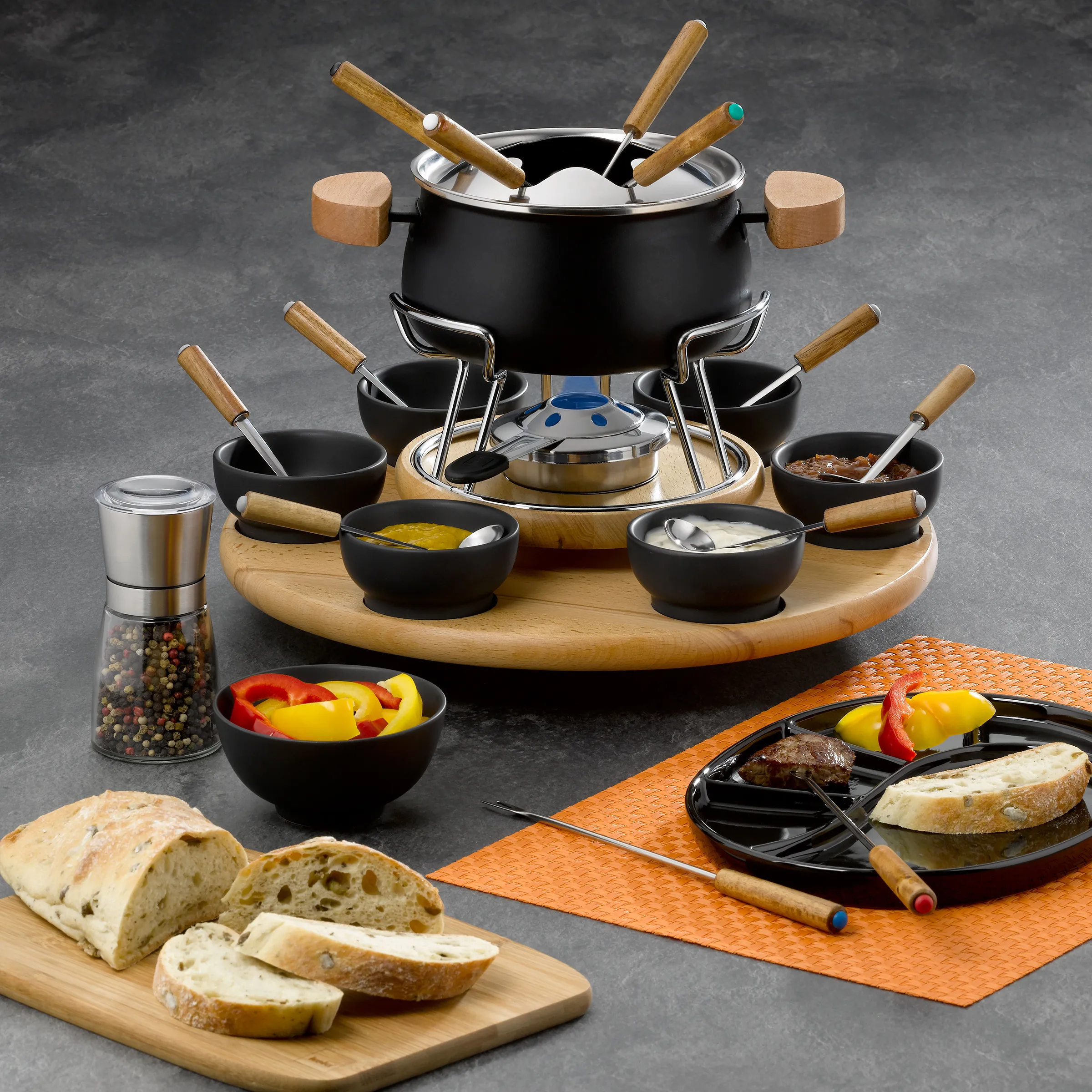 Fondue-Set: Komplettes Fondue-Service mit Topf und Zubehör Fondue-Set mit schwarzem Topf, Holzständer, mehreren kleinen Schüsseln, Fondue-Gabel und Zutaten wie Brot und Gemüse.