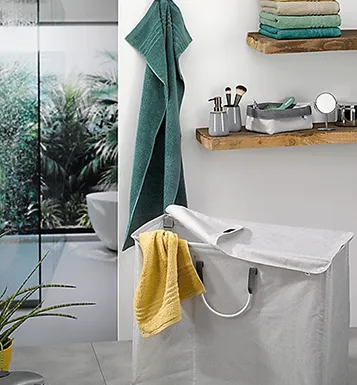 Modernes Badezimmer mit freistehender weißer Badewanne, grünem und gelbem Handtuch, Holzregalen mit Accessoires und Pflanzendekoration
