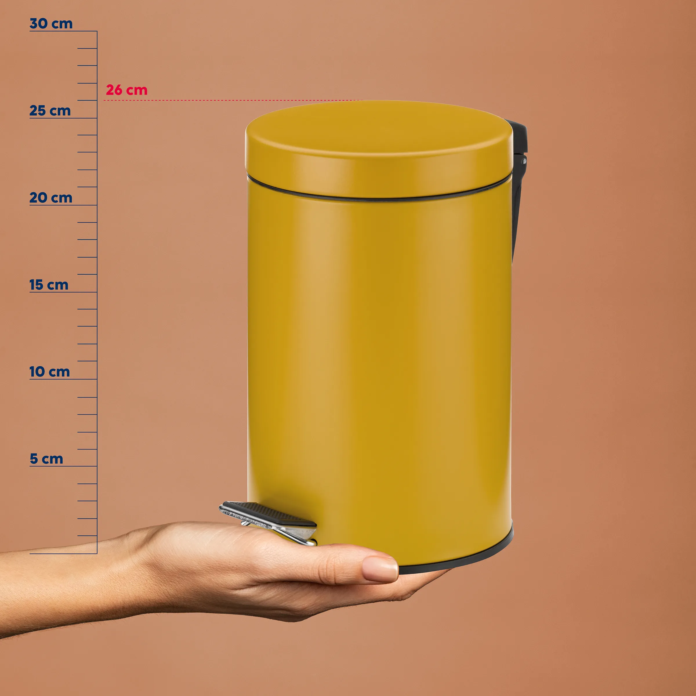 Gelber Treteimer 26 cm - kompakter Mülleimer Gelber Treteimer mit schwarzem Deckel und Griff, neben einer Hand vor Größenskala von 5-30 cm