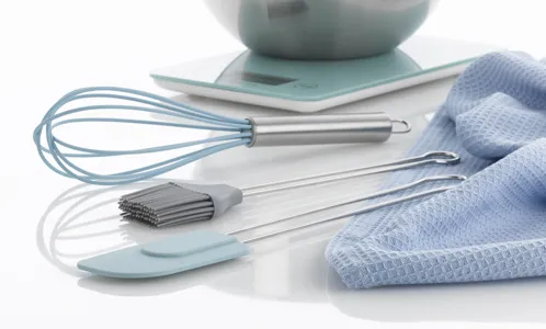 Küchenutensilien Set mit Schneebesen, Spatel und Pastabürste neben blauem Küchentuch und Schüssel
