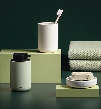 Badezimmer-Accessoires-Set mit Zahnbürstenhalter, Seifenschale und Handtüchern auf grünem Hintergrund