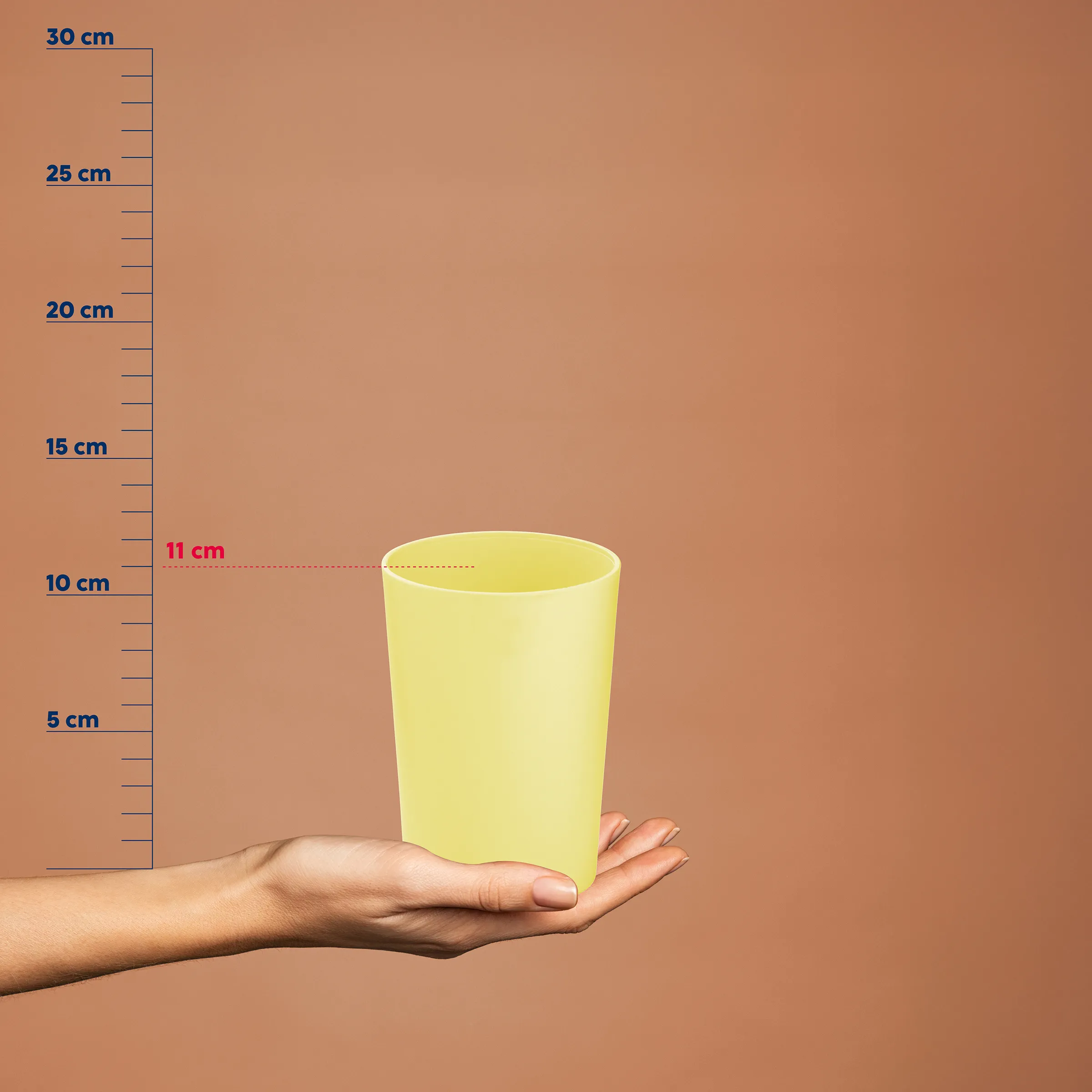 Gelber Kunststoffbecher in einer Hand mit Messskala, zeigt eine Höhe von etwa 11 cm Füllstand