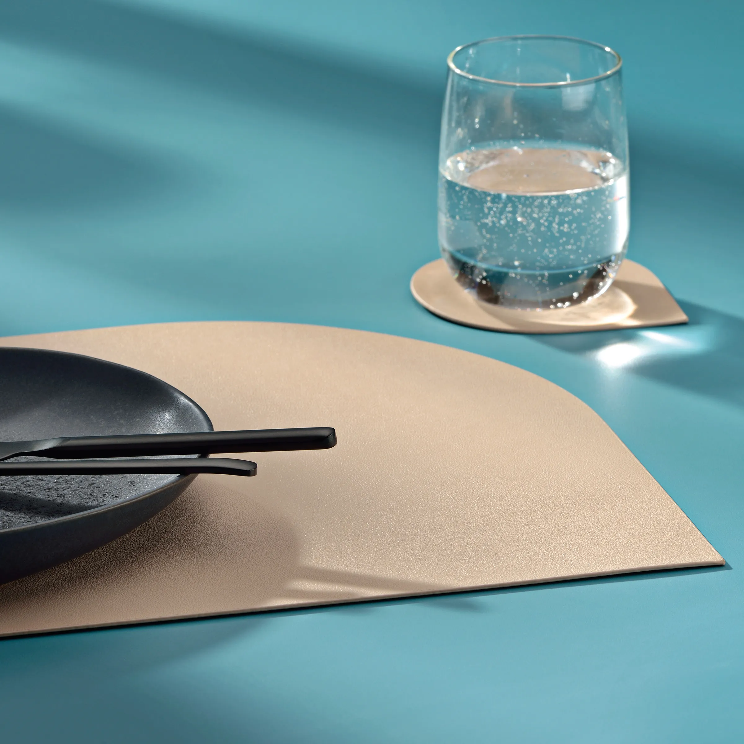 Moderne Tischdeckung und Esskultur Design Minimalistische Tischkulisse mit schwarzem Teller, Stäbchen, beiger Platzdecke und Glas Wasser auf blauem Untergrund