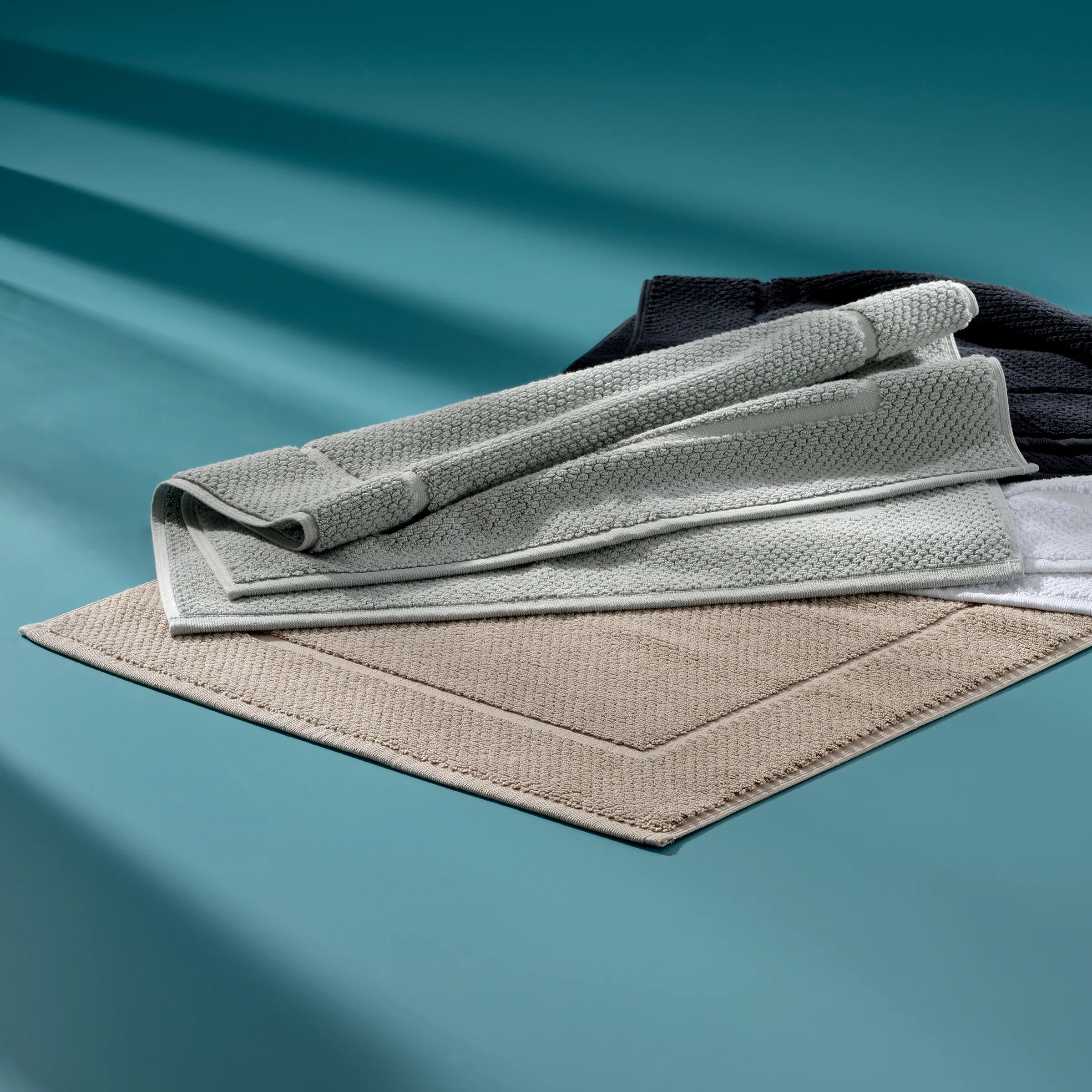 Stapel aus verschiedenfarbigen Handtüchern in Beige, Grau, Weiß und Dunkelblau auf blauem Hintergrund