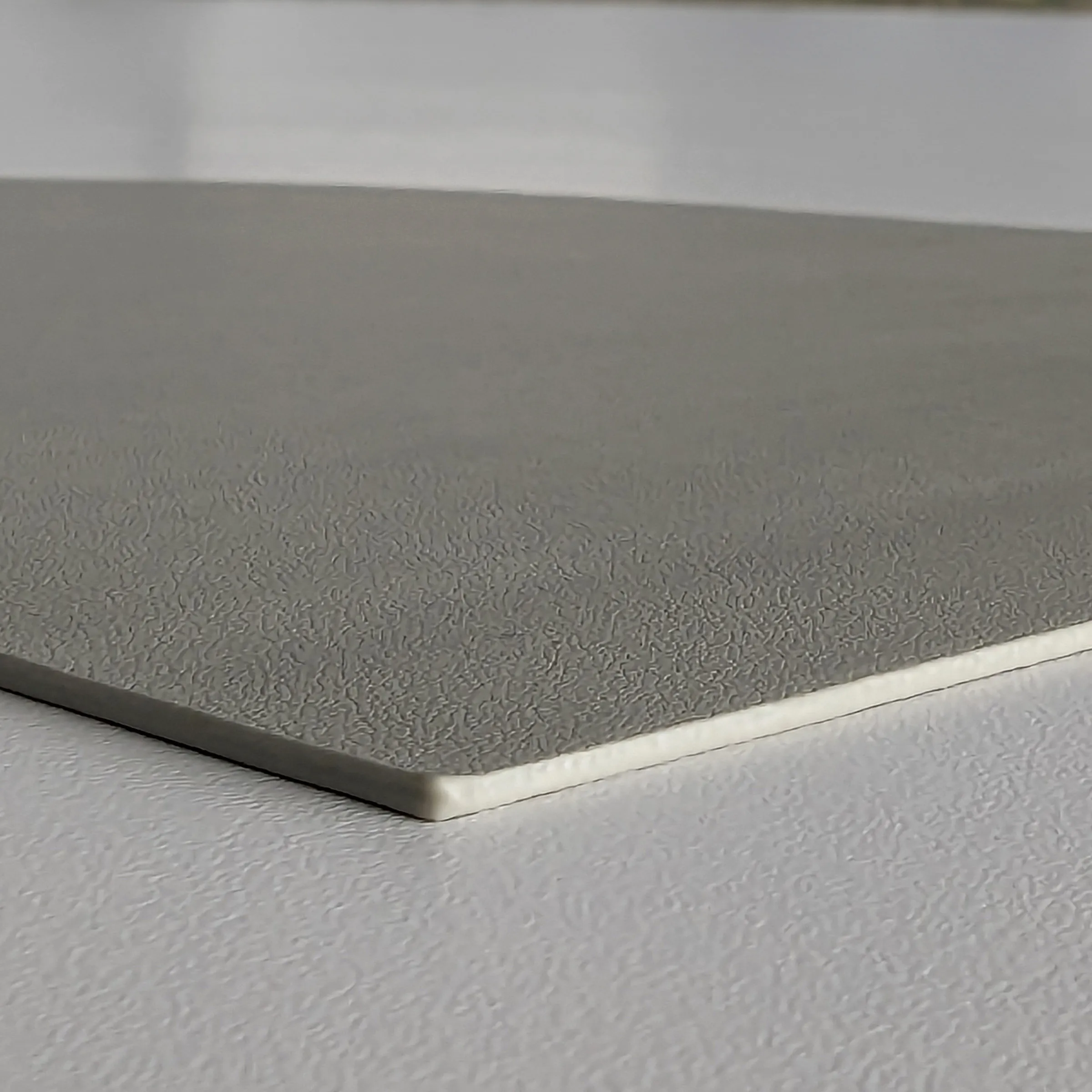 Strukturierte Kunststoffplatte grau mit texturierter Oberfläche Graue Kunststoffplatte mit strukturierter Oberfläche und weißer Kante im Detail
