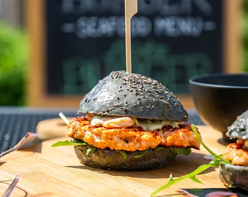Premium Burger mit Hähnchen - Gourmet Fastfood Gourmet-Burger mit schwarzem Sesambrötchen, saftiger Patty und crispy Hähnchen-Topping auf Holzbrett
