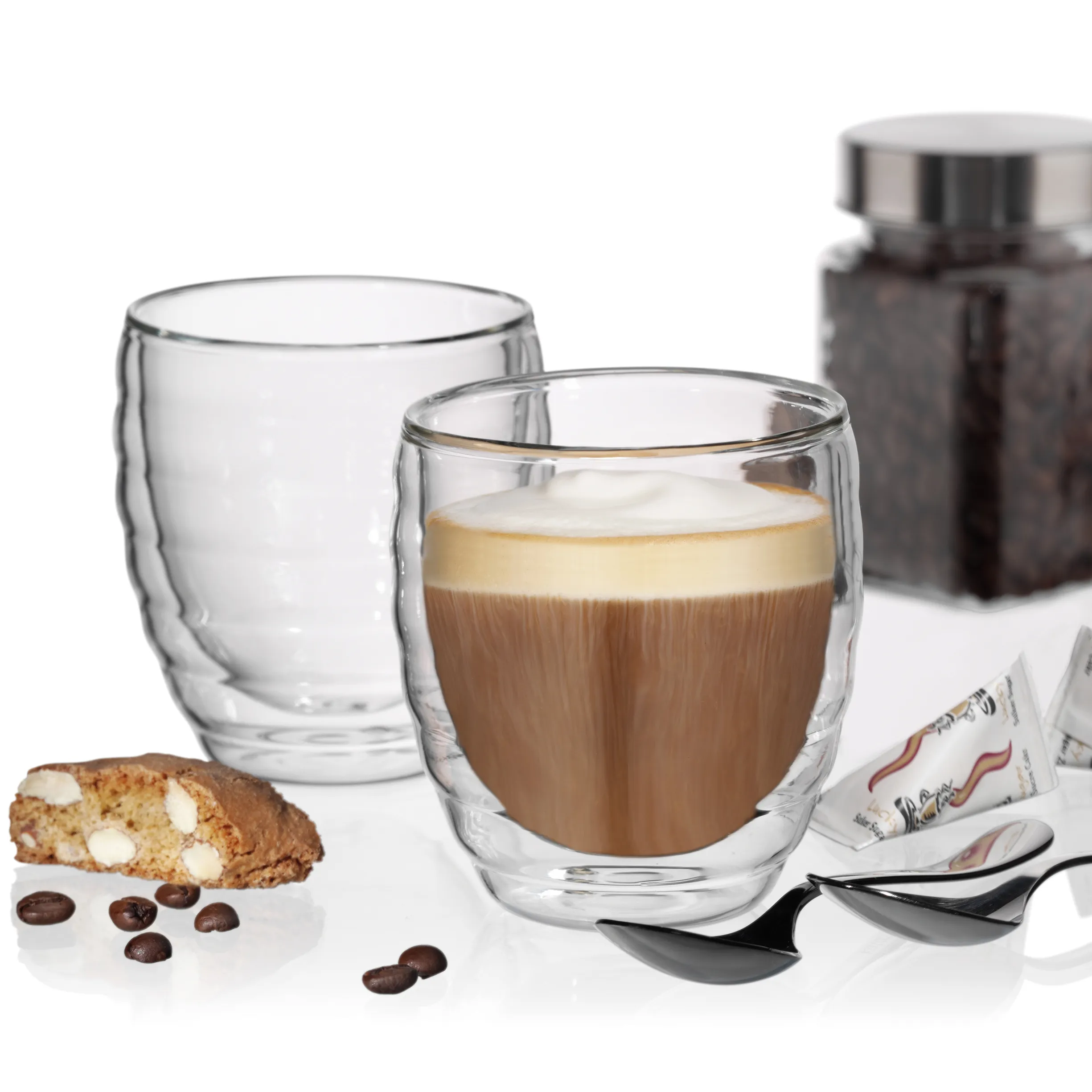Doppelwandige Kaffeegläser Set mit Cappuccino und Barista-Zubehör Doppelwandige Gläser mit Cappuccino, Kaffeedose, Biscotti und Kaffeebohnen auf weißem Hintergrund
