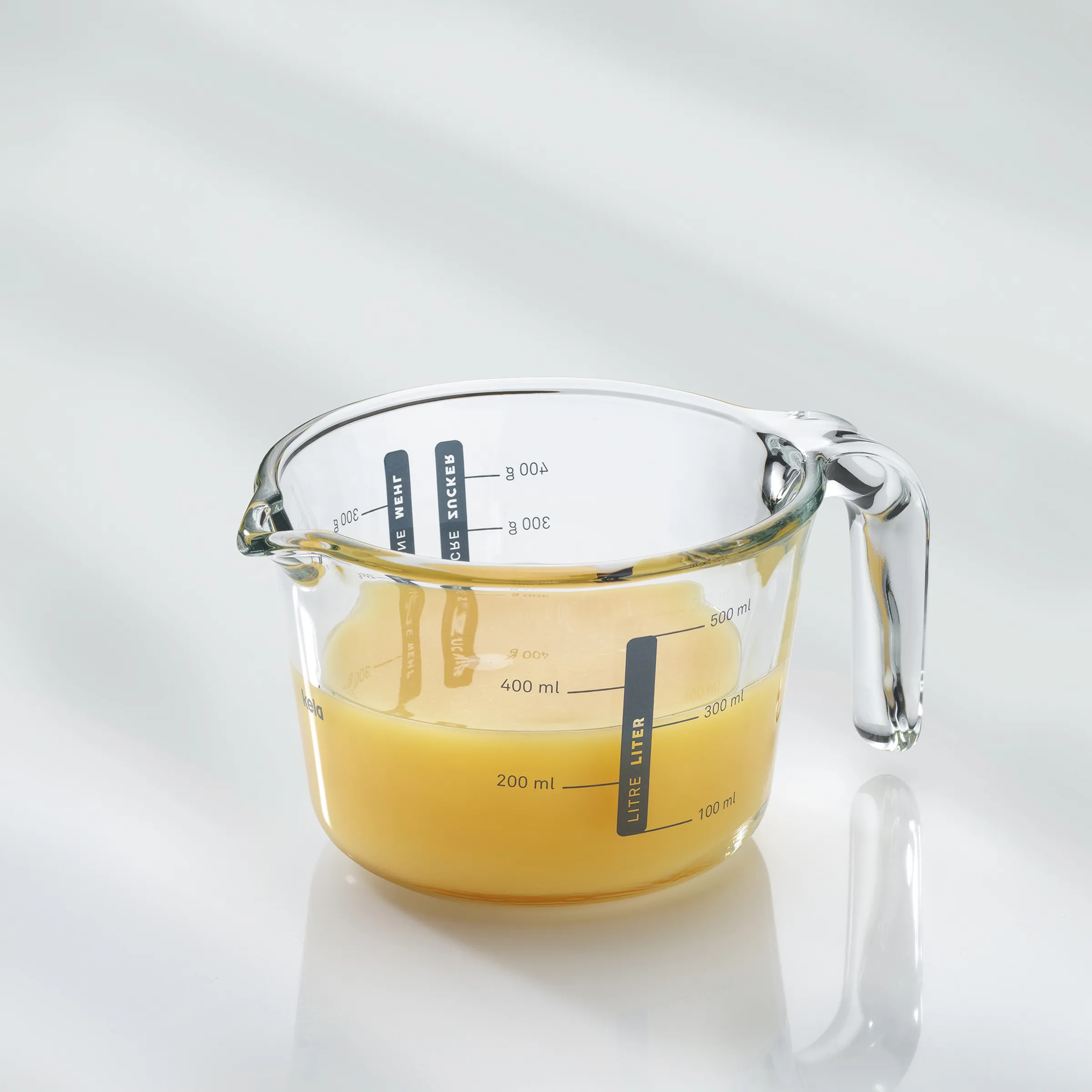 Glas-Messbecher mit 500ml gelblicher Flüssigkeit, Skala und Henkel auf weißem Hintergrund