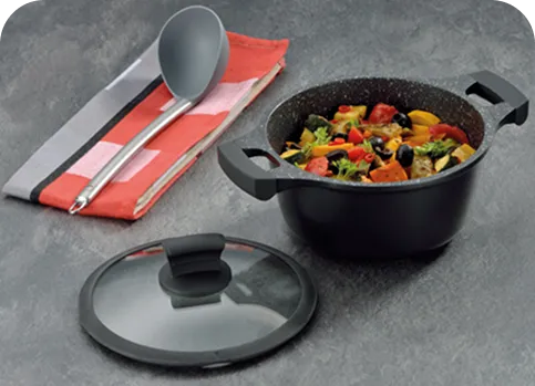 Kochtopf-Set mit Glasdeckel und Kochbesteck - Antihaft-Beschichtung für gesundes Kochen Schwarzer Kochtopf mit Glasdeckel und buntem Gemüse, daneben Serviette mit Kochlöffel auf grauer Arbeitsfläche