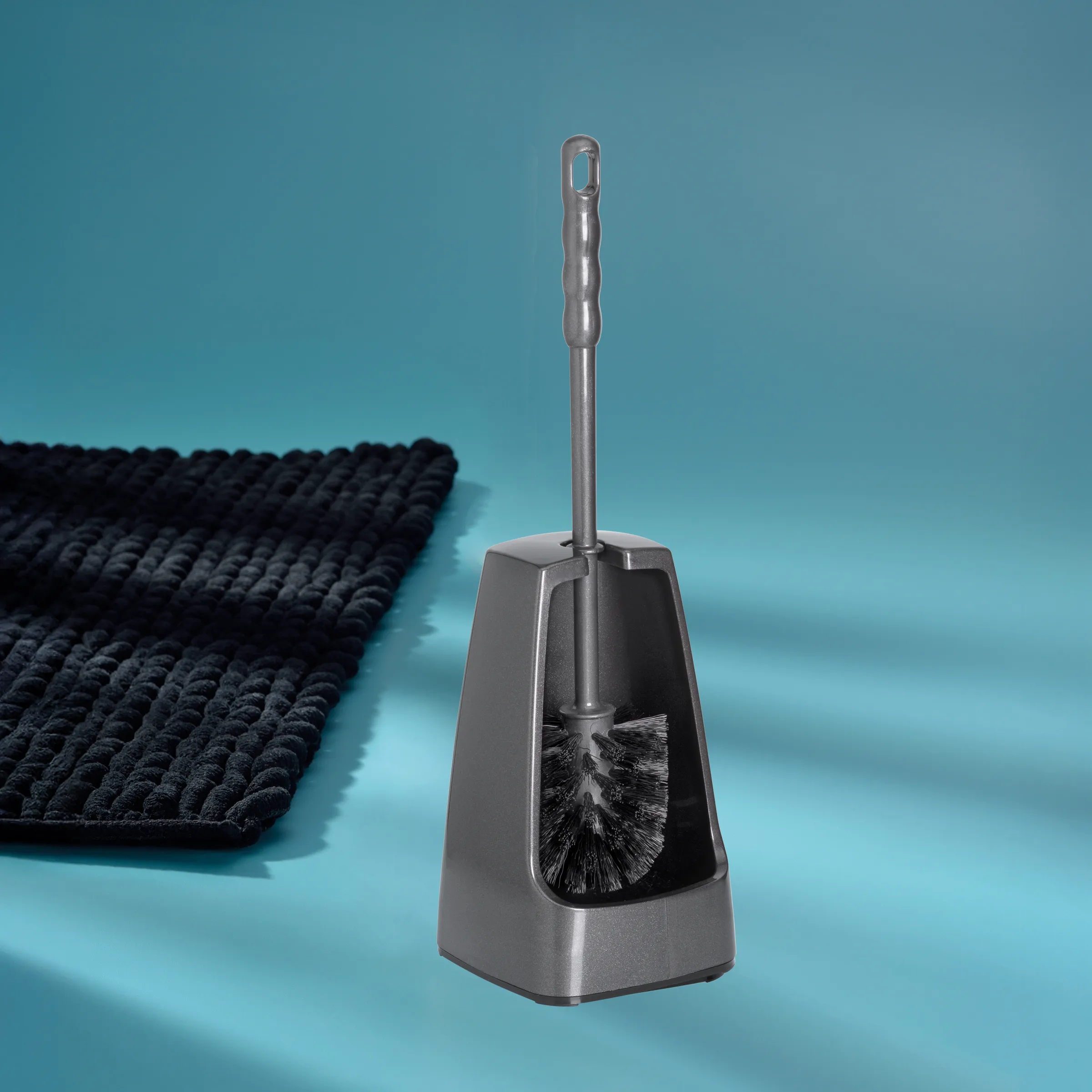 Toilettenbürste mit Halter - Badezimmer Reinigungsbürste Schwarze Toilettenbürste mit grauem Kunststoffhalter auf hellblauem Hintergrund neben schwarzer Badematte