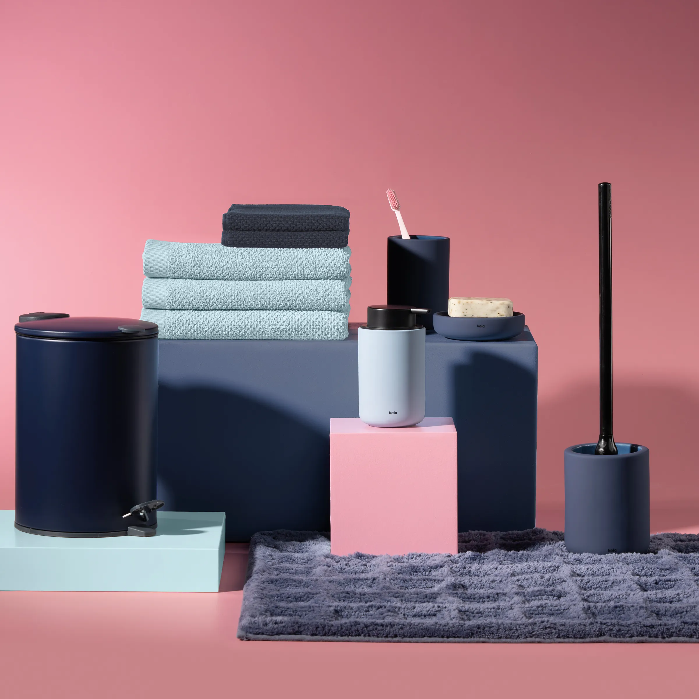 Badezimmer-Accessoires Set - moderne Deko-Kollektion Moderne Badezimmer-Accessoires-Kollektion mit hellblauen Handtüchern, dunklen Behältern und schwarzem Toilettenbürsten-Set auf rosa Hintergrund