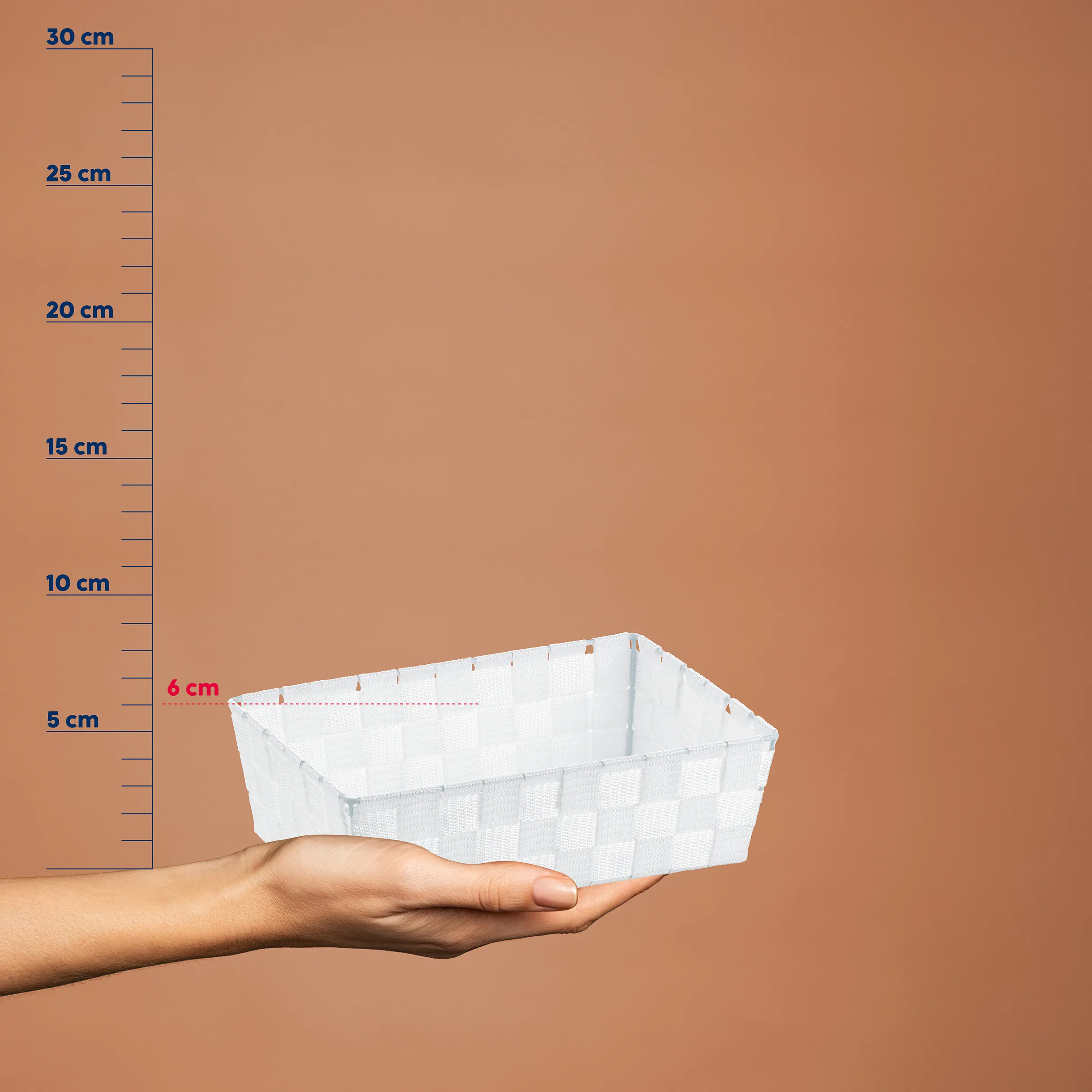 Weiße Aufbewahrungsbox mit Maßstab links, Höhe etwa 6 cm, in einer Hand auf beigem Hintergrund