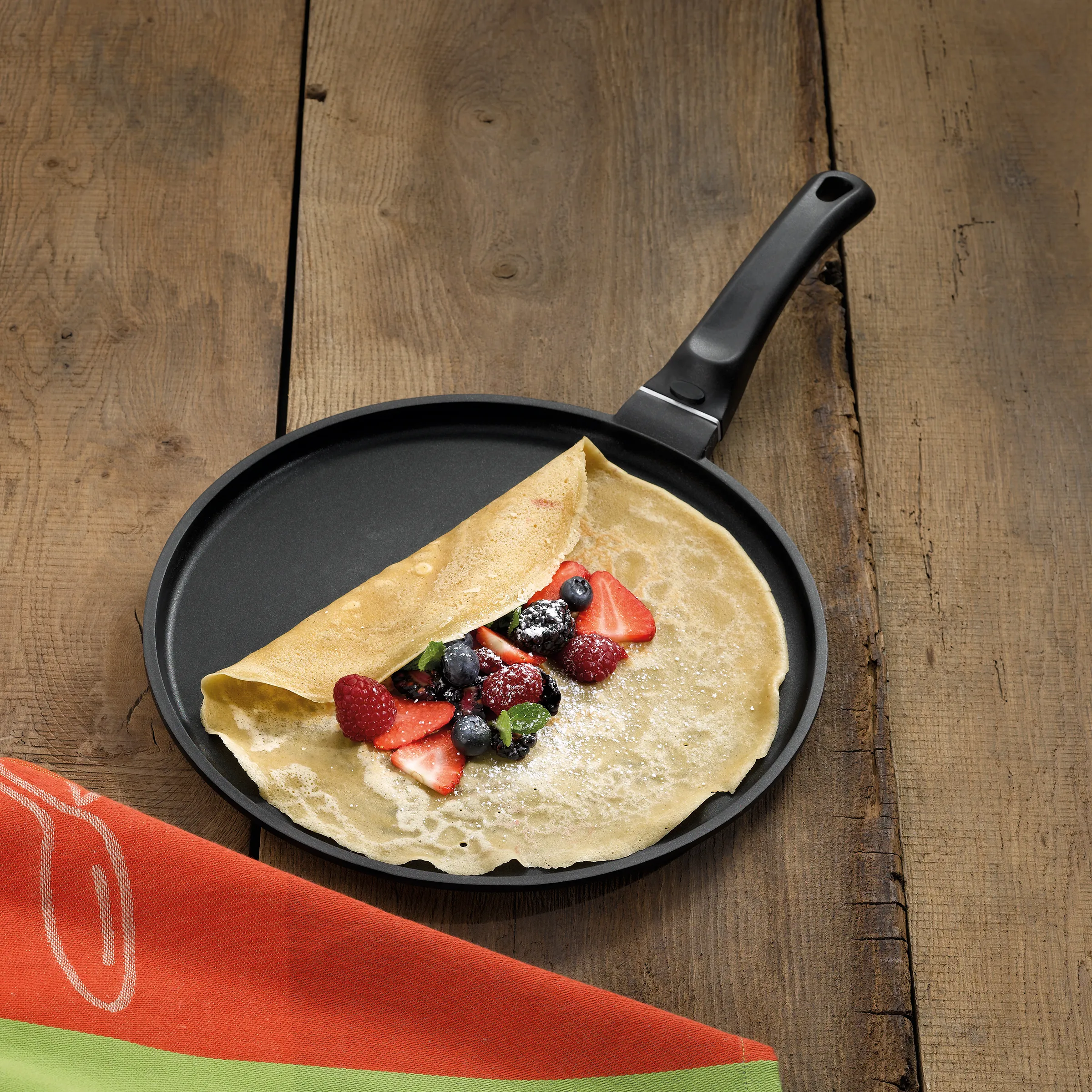 Crêpe mit Beeren - süße Crepe Pfanne Crêpe in schwarzer Pfanne mit Erdbeeren, Himbeeren und Blaubeeren, garniert mit Puderzucker