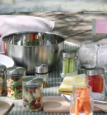 Edelstahlschüssel mit Lebensmittel-Aufbewahrungsgläsern Große Edelstahlschüssel mit Lebensmittelvorräten in Gläsern: Salat, Gemüse und Flüssigkeiten auf Arbeitstisch.