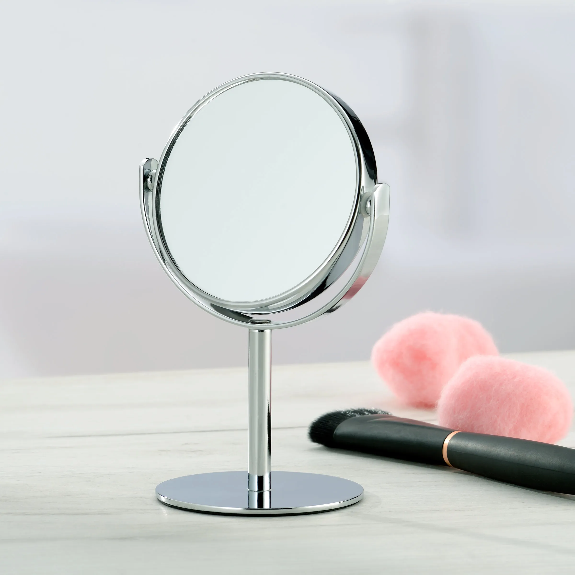 Kosmetikspiegel Chrom Stand-Schminkspiegel mit doppelseitiger Vergrößerung Runder Kosmetikspiegel mit Chrombeschichtung auf Standfuß neben rosa Make-up-Schwämmen und Pinsel