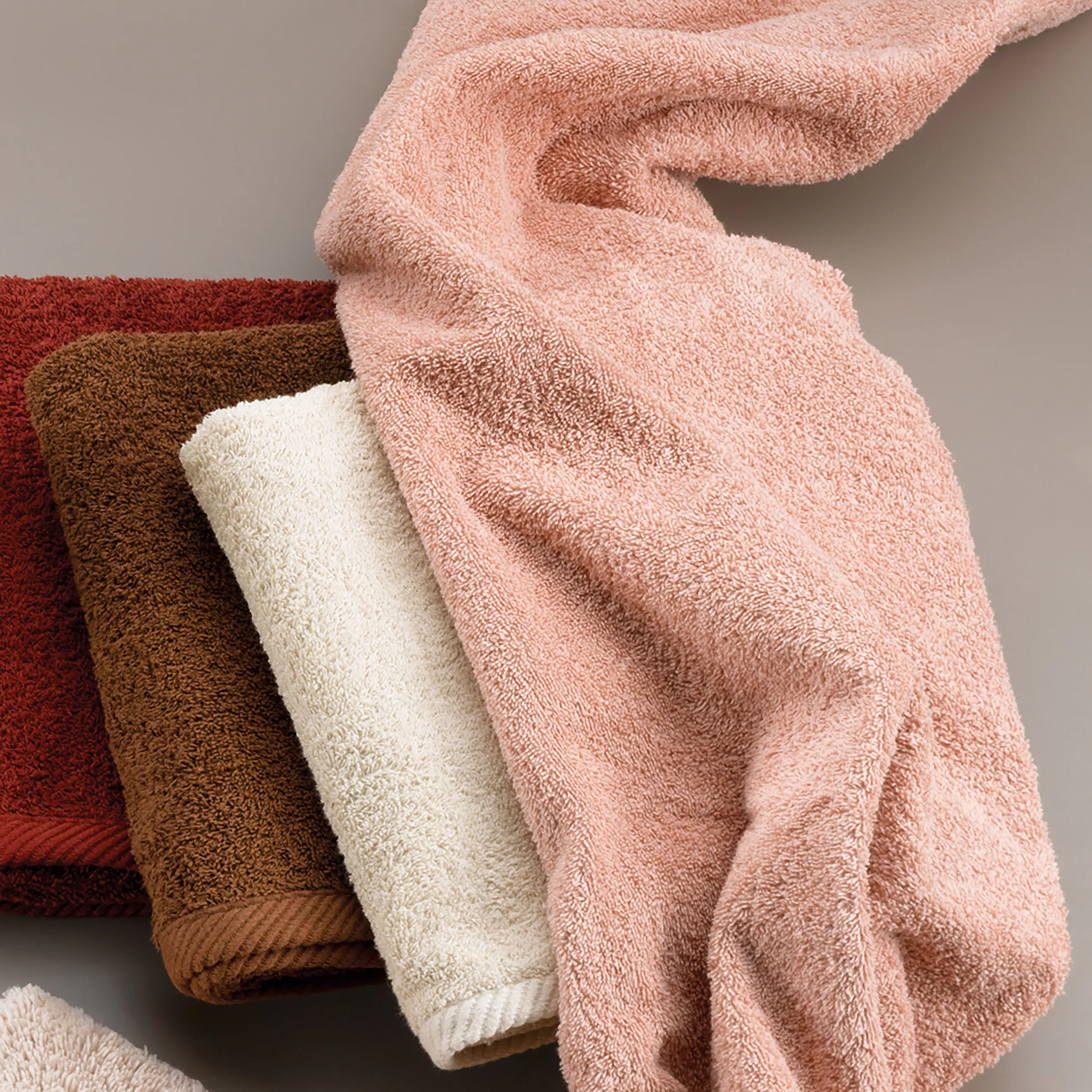 Hochwertige Frotteehandtücher in verschiedenen Farben Stapel aus vier weichen Frotteehandtüchern in den Farben Rot, Braun, Creme und Rosa mit sichtbarer Textur