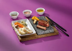 Sushi-Set mit Nigiri, Reis und Dips - Japanisches Gericht auf Holzbrett Sushi-Platte mit Lachs-Nigiri, Reis, Gemüse und drei Dip-Schalen auf Holzbrett mit Stäbchen auf violettem Hintergrund