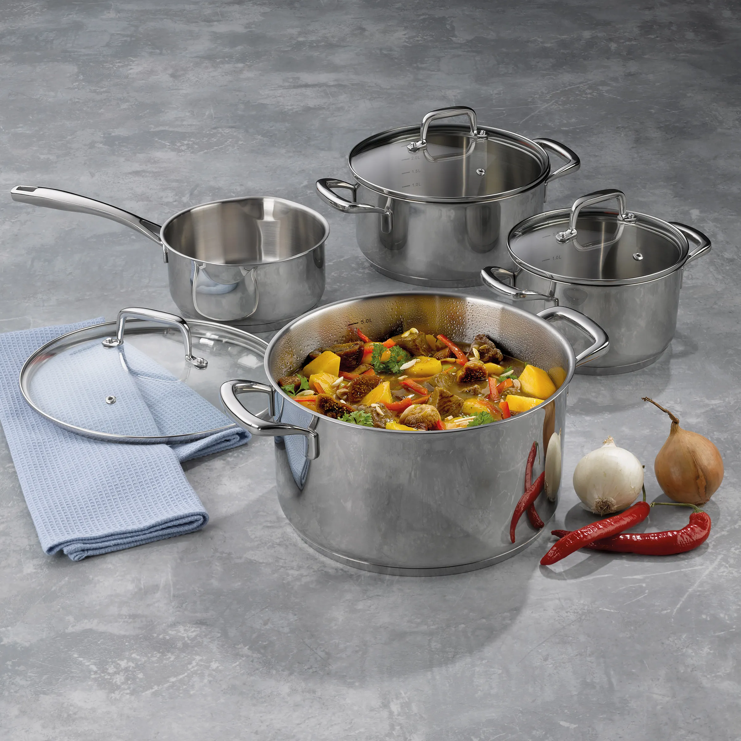 Edelstahl-Kochgeschirr-Set mit 5-teilig: großem Topf mit Gemüseeintopf, Saucen- und Kochtöpfen, blauem Tuch und frischem Gemüse