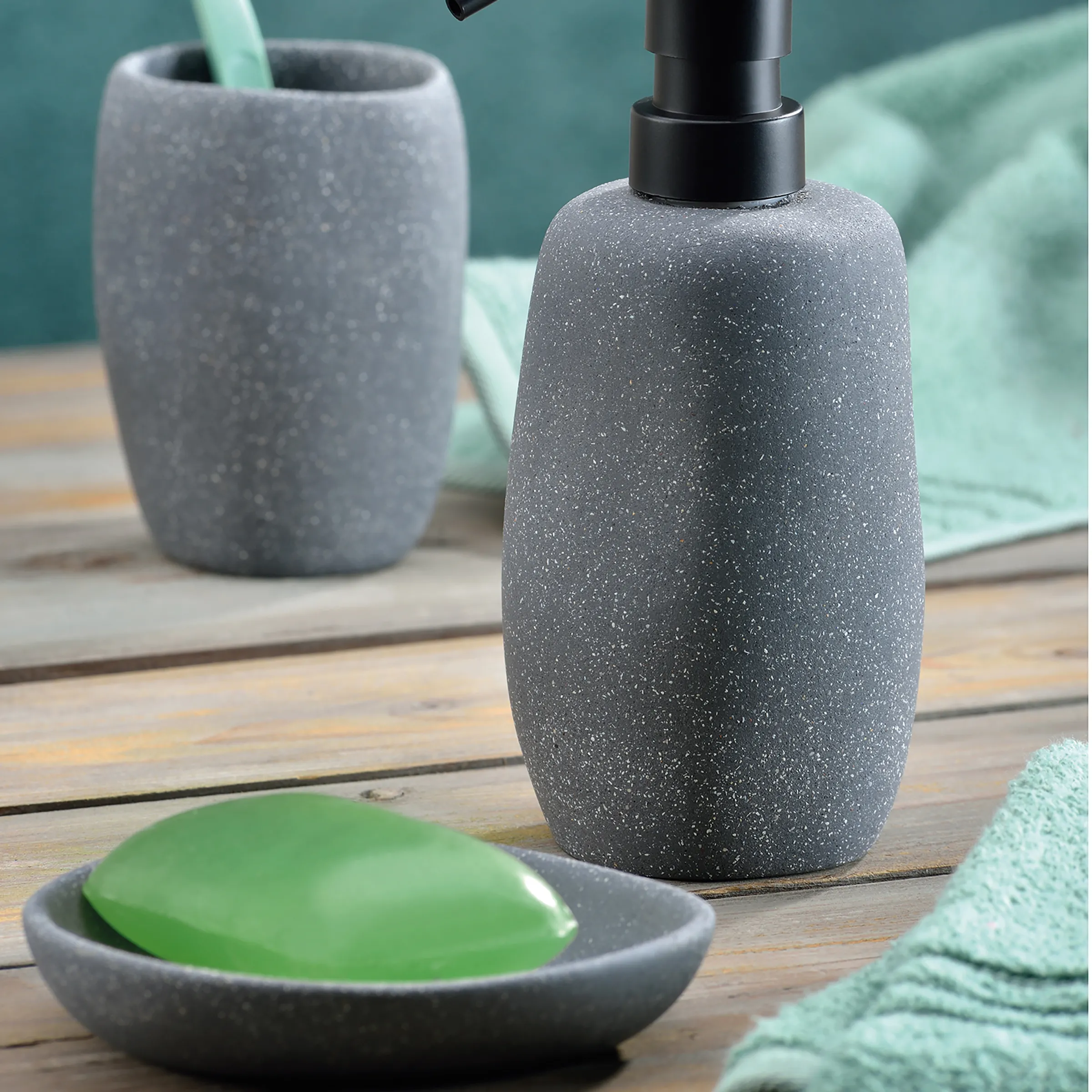 Badezimmer Zubehör Set aus grauem Beton mit Seifenspender Graues Badezimmer-Set mit Seifenspender, Zahnputzbecher und grüner Seife auf Holztisch