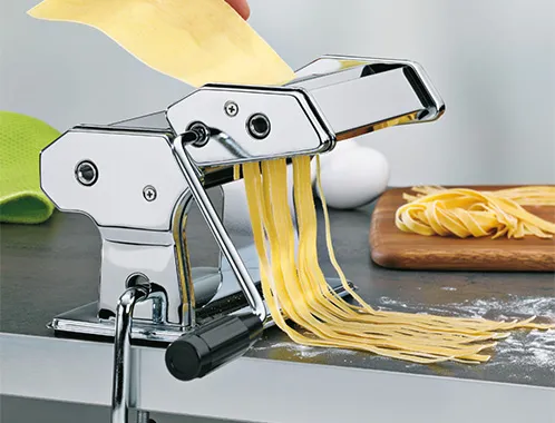 Nudelmaschine Edelstahl - Pasta Maker für frische Nudeln Edelstahl-Nudelmaschine mit ausgerolltem gelben Nudelteig auf Holzbrett, Zutaten im Hintergrund
