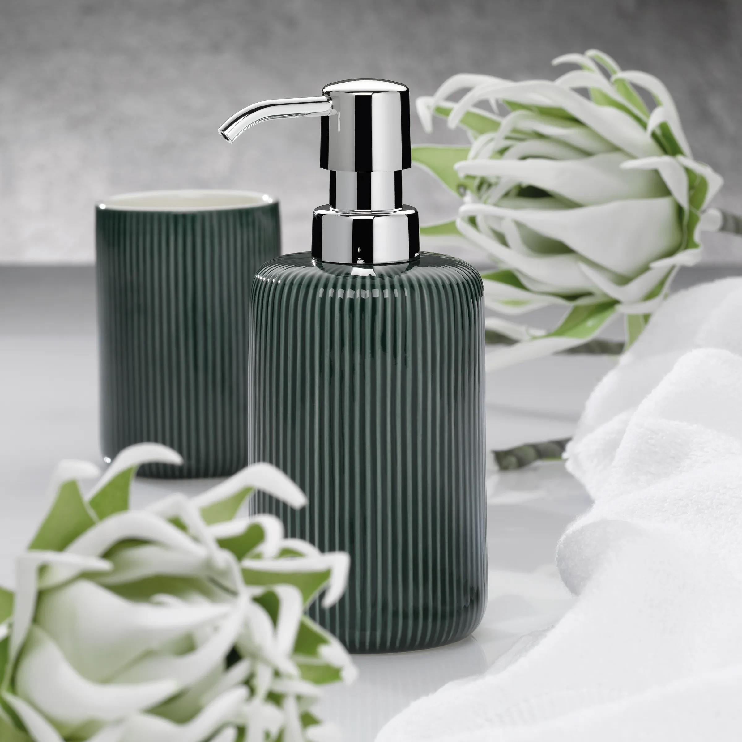 Badezimmer Set Seifenspender Keramik grün Grüne Seifenspender und Zahnputzbecher mit gerilltem Design neben weißen Blüten auf grauem Untergrund