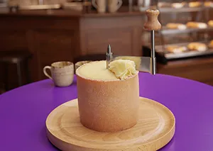 Mousse-Torte Dessert auf Holzteller - Feine Patisserie Elegantes Dessert auf Holzteller mit violettem Tisch, cremige Mousse-Torte mit weißer Dekoration