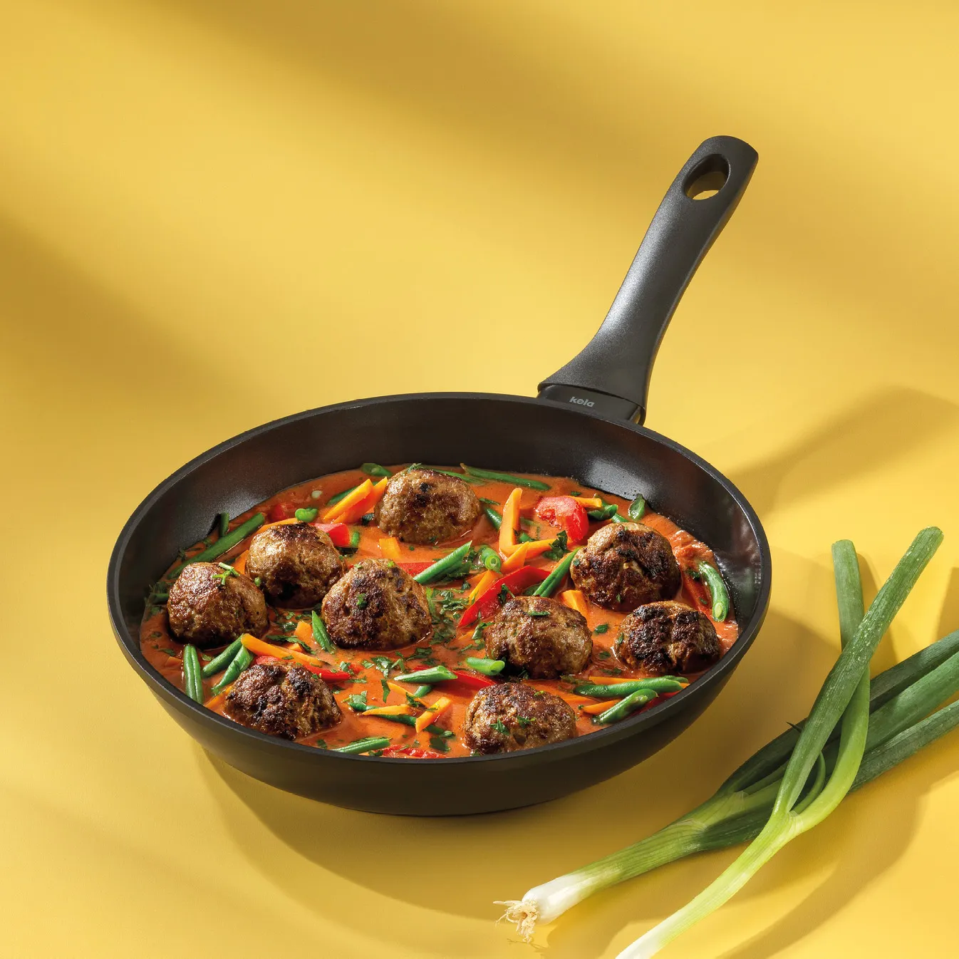 Schwarze Pfanne mit köstlichen Fleischbällchen in roter Tomatensauce, grünen Bohnen und Paprika auf gelbem Hintergrund