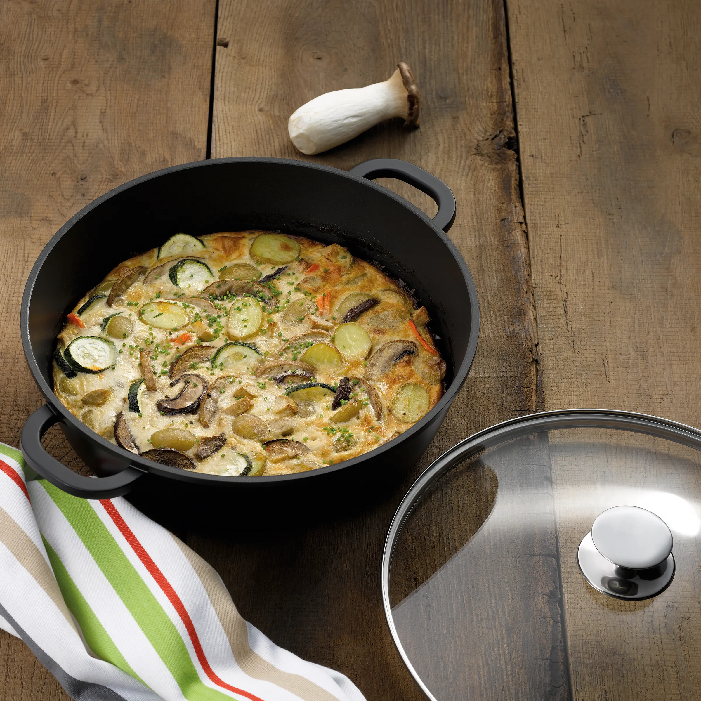Gemüse-Frittata in Bratpfanne - Rezept mit Zucchini und Pilzen Gemüse-Frittata mit Zucchini, Pilzen und Kartoffeln in schwarzer Bratpfanne auf Holztisch