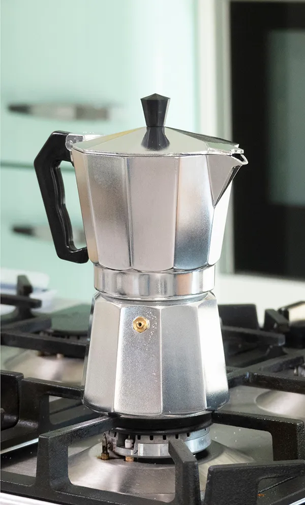 Espressokanne auf Gasherd - Italienischer Mokka-Kaffeebereiter aus Aluminium Silberne Espressokanne mit schwarzem Griff auf Gasherd in moderner Küche