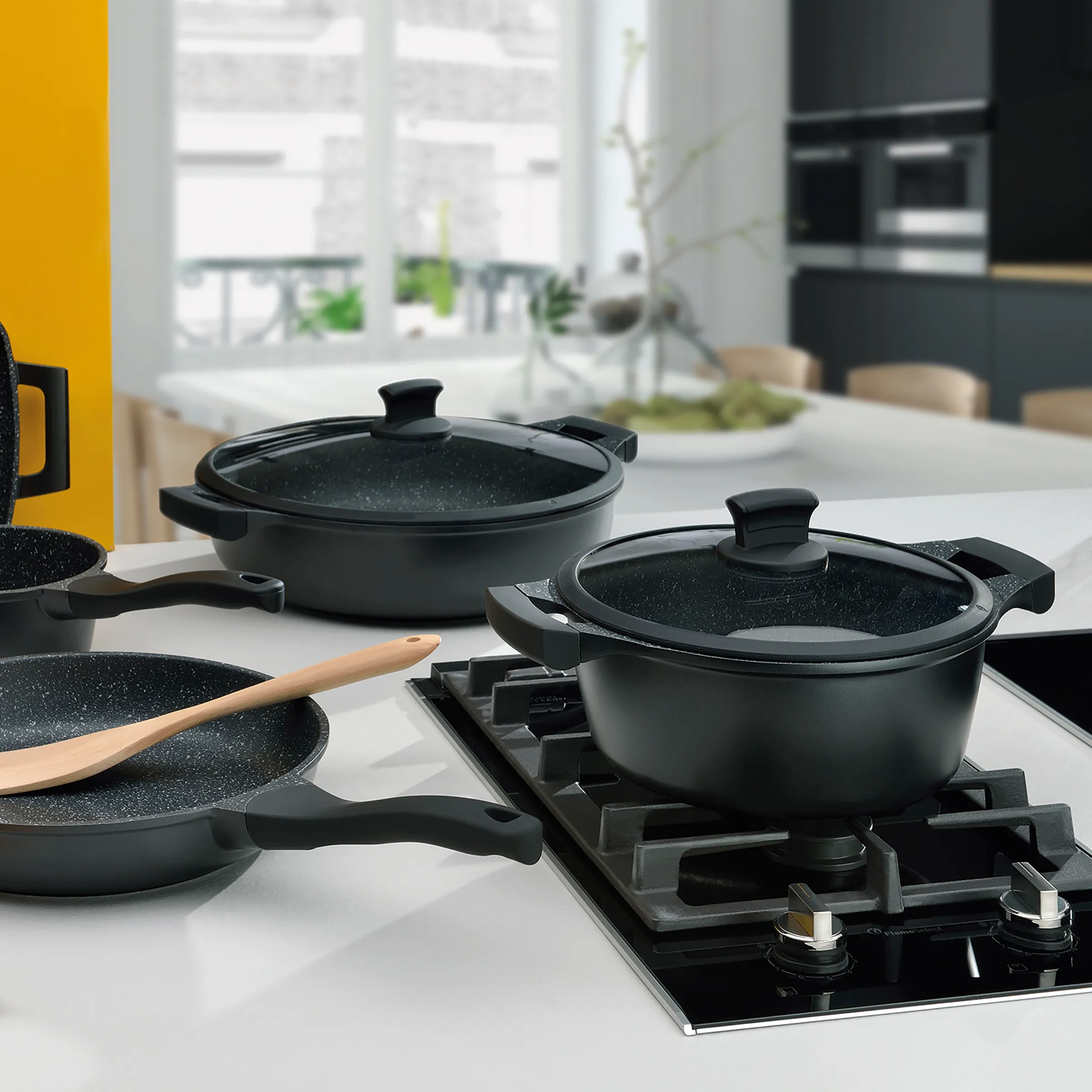 Kochgeschirr-Set mit Antihaftbeschichtung - Töpfe und Pfannen für moderne Küchen Schwarzes Kochgeschirr-Set mit Marmorbeschichtung auf Gasherd in moderner Küche mit gelbem Akzent
