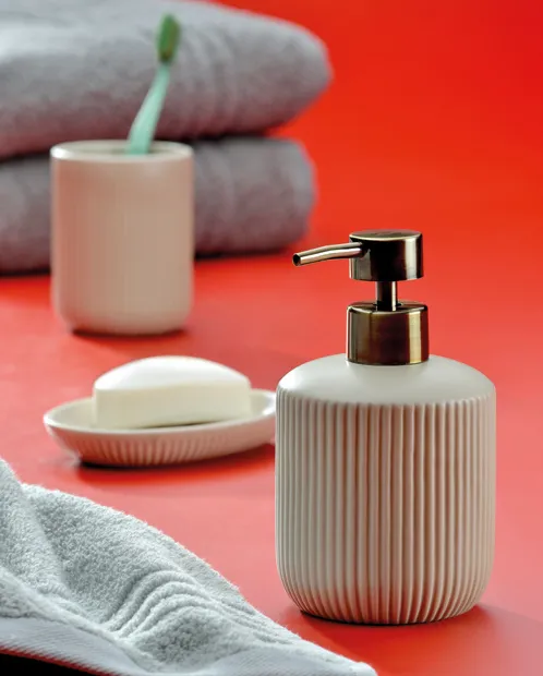 Badezimmer-Set in Rosa mit Seifenspender, Zahnputzbecher und Seifenschale auf rotem Hintergrund mit Handtuch