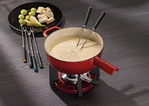 Fondue-Set mit Käsefondue – Rotes Fondue-Geschirr mit Gabeln und Beilagen Rotes Fondue-Set mit Käsefondue, Gabeln und Beilagen wie Brot, Kartoffeln und Gemüse auf dunklem Holztisch